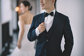 an asian chinese wedding couple standing at the corridor with full suit and wedding dress smiling focusing on bridegroom
