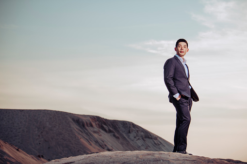 an asian chinese handsome well dressed man looking away at the desert with hand in the pocket in the evening