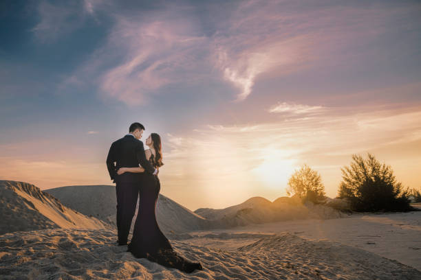 劇的な空と日没の間にメラカ砂丘でアジアの中国のカップルの結婚式の肖像画セッション - weding gown ストックフォトと画像