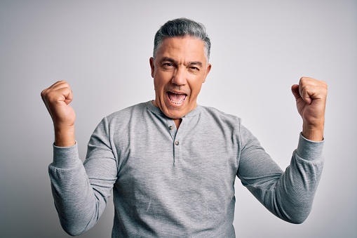 Middle age handsome grey-haired man wearing casual t-shirt over white background celebrating surprised and amazed for success with arms raised and open eyes. Winner concept.