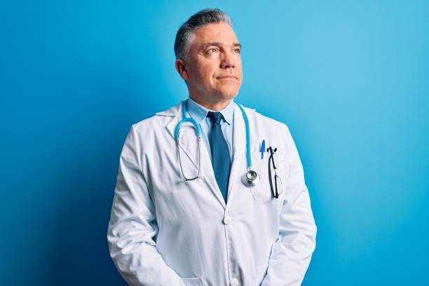 middle age handsome grey-haired doctor man wearing coat and blue stethoscope smiling looking to the side and staring away thinking. - mannered imagens e fotografias de stock