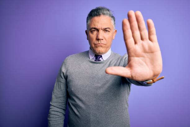 istock Middle age handsome grey-haired man wearing elegant sweater over purple background doing stop sing with palm of the hand. Warning expression with negative and serious gesture on the face. 1212692271