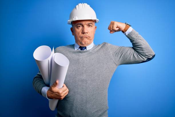 istock Middle age handsome grey-haired architect man wearing safety helmet holding blueprints Strong person showing arm muscle, confident and proud of power 1212692553