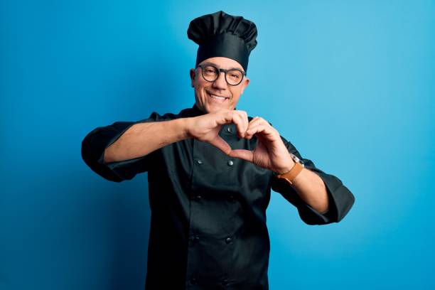 istock Middle age handsome grey-haired chef man wearing cooker uniform and hat smiling in love doing heart symbol shape with hands. Romantic concept. 1212692554