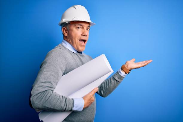 istock Middle age handsome grey-haired architect man wearing safety helmet holding blueprints pointing aside with hands open palms showing copy space, presenting advertisement smiling excited happy 1212692566