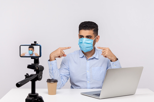News reporter pointing at medical face mask and broadcasting about coronavirus, making video giving tips on using protect filter against contagious disease, 2019-ncov, flu outbreak. indoor studio shot