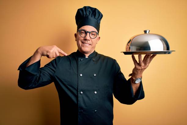istock Middle age handsome grey-haired waiter man wearing cooker uniform and hat holding tray looking confident with smile on face, pointing oneself with fingers proud and happy. 1212692997