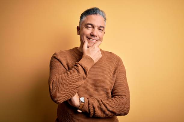 istock Middle age handsome grey-haired man wearing casual sweater over yellow background looking confident at the camera smiling with crossed arms and hand raised on chin. Thinking positive. 1212693110