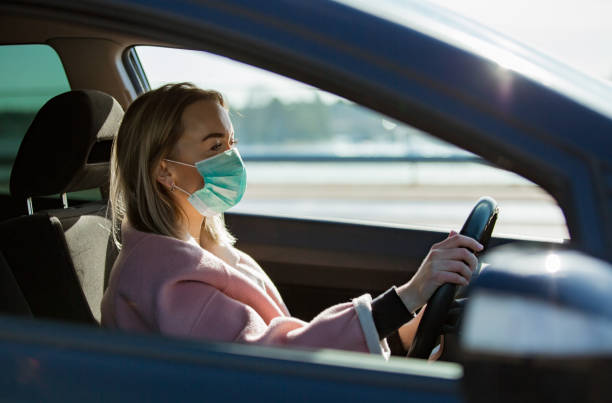 istock Woman in protective mask driving a car on road. 1212696723