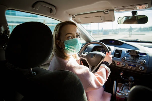 istock Woman in protective mask driving a car on road. 1212697871
