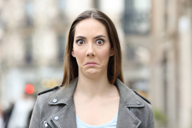 Shocked woman looking at camera on city street Front view portrait of a shocked young woman looking perplexed at camera on city street funny shock stock pictures, royalty-free photos & images