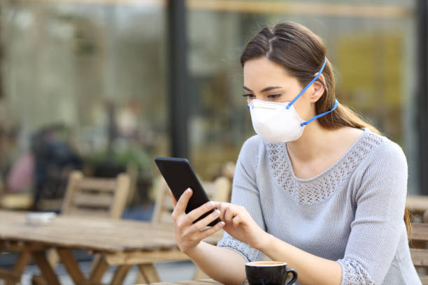 istock Woman with protective mask looking at phone on a cafe 1212698307