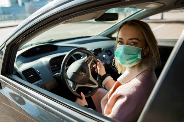 donna in maschera protettiva alla guida di un'auto su strada. - driving women rear view sitting foto e immagini stock