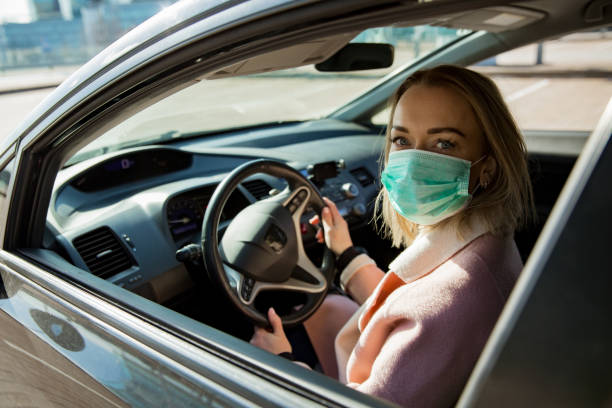 Woman in protective mask driving a car on road.
