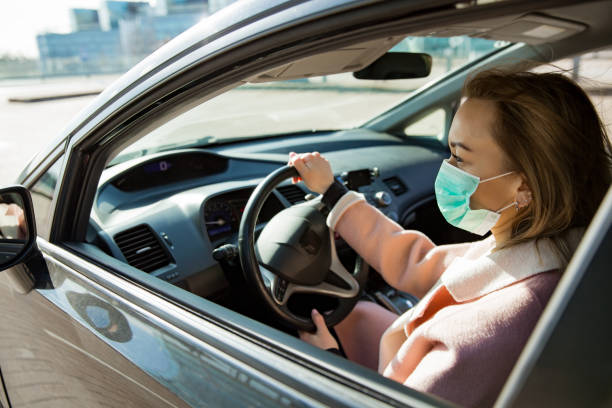 istock Woman in protective mask driving a car on road. 1212698488