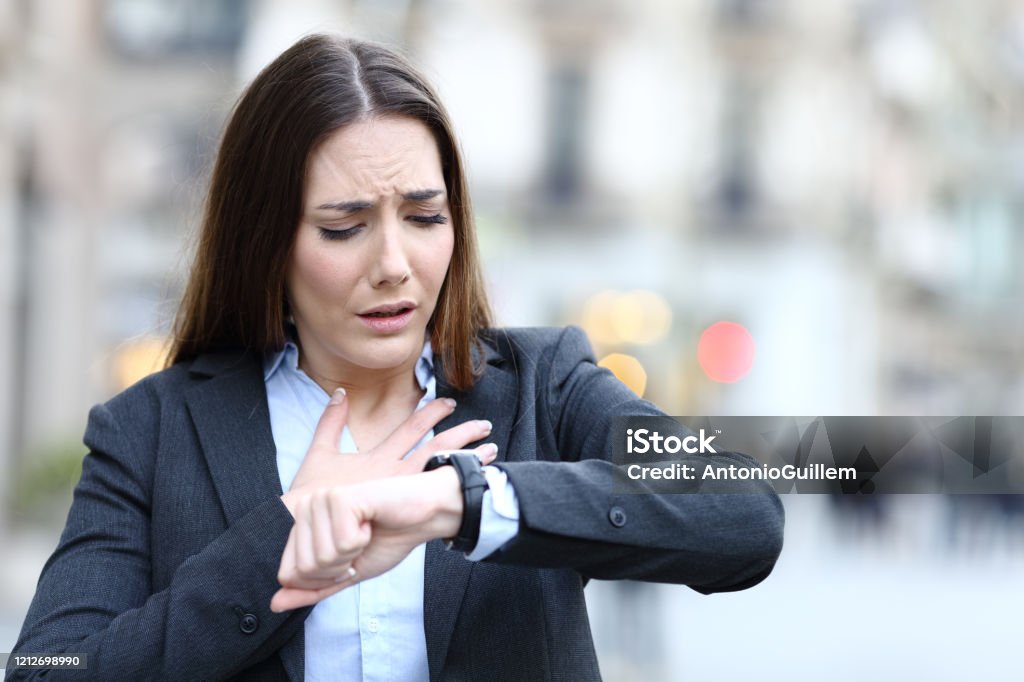 Worried executive checking heart rate on smart watch Front view portrait of worried executive monitoring heart rate on smart watch on city street Inhaling Stock Photo