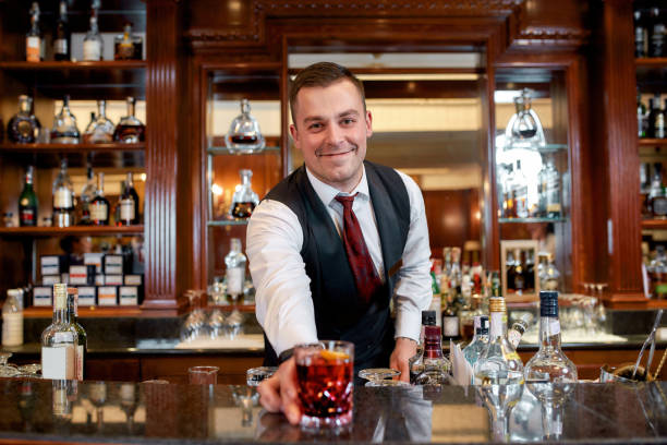 istock Your drink is ready. Young bartender standing at counter, smiling and presenting iced cocktail in the glass 1212699699
