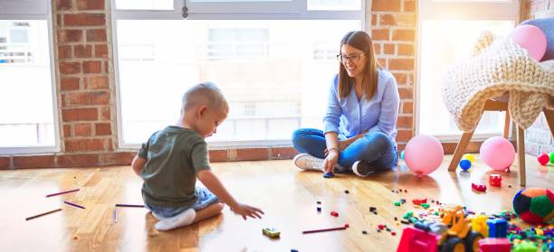 junge skaukasische kind spielen in der spielschule mit lehrer. mutter und sohn beim spielzimmerrennen mit spielzeugautos - child playroom parent indoors stock-fotos und bilder