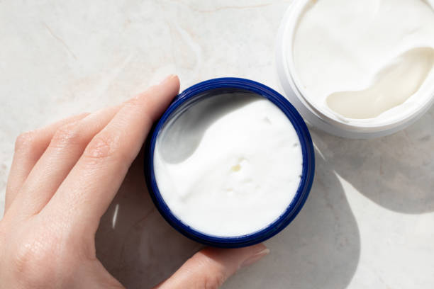 Girl hand holding face cream, close-up. Moisturizer in container on marble background, top view. Skincare stock photo