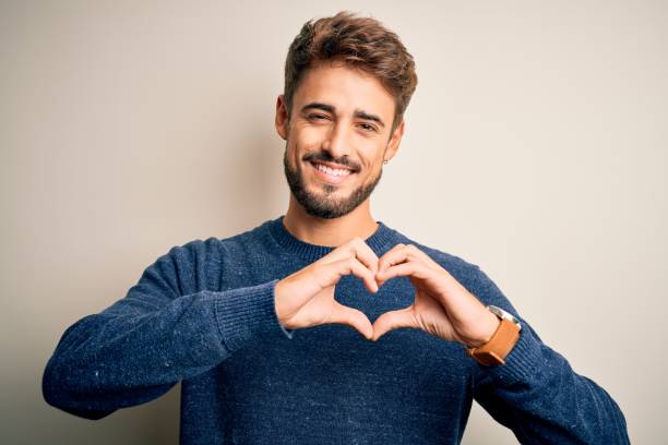 young handsome man with beard wearing casual sweater standing over white background smiling in love showing heart symbol and shape with hands. romantic concept. - made man object imagens e fotografias de stock