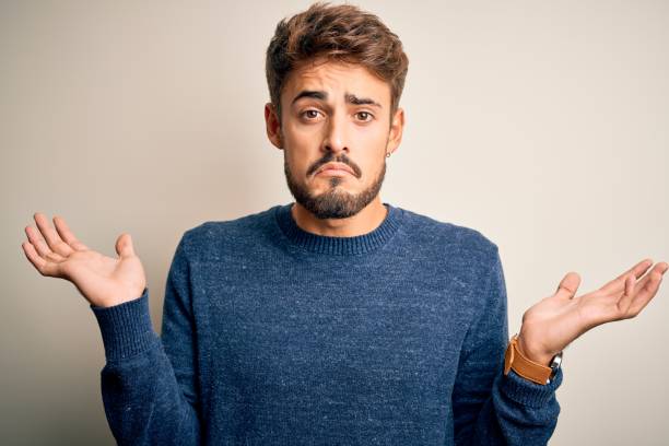 istock Young handsome man with beard wearing casual sweater standing over white background clueless and confused expression with arms and hands raised. Doubt concept. 1212701646