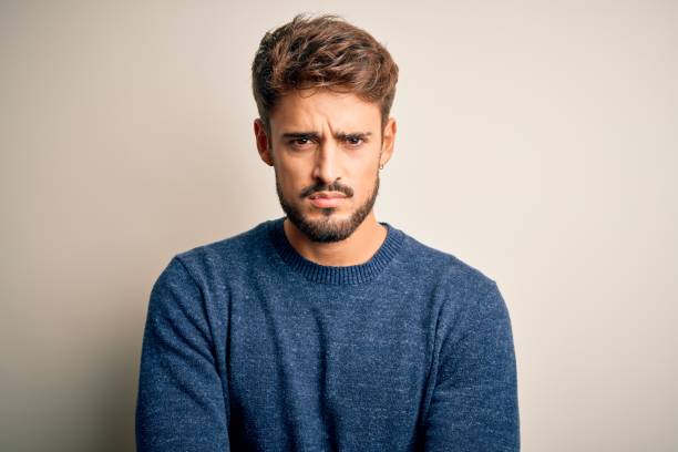 istock Young handsome man with beard wearing casual sweater standing over white background skeptic and nervous, disapproving expression on face with crossed arms. Negative person. 1212701721