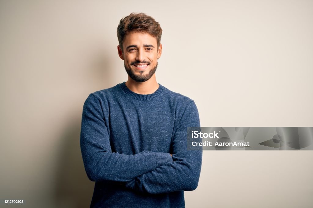 Junger stattliche Mann mit Bart trägt lässigen Pullover stehend über weißem Hintergrund glückliches Gesicht lächelnd mit gekreuzten Armen blickend in die Kamera. Positive Person. - Lizenzfrei Männer Stock-Foto