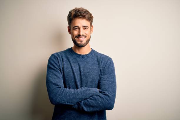 giovane bell'uomo con la barba che indossa un maglione casual in piedi sopra sfondo bianco faccia felice sorridente con le braccia incrociate guardando la macchina fotografica. persona positiva. - young men foto e immagini stock