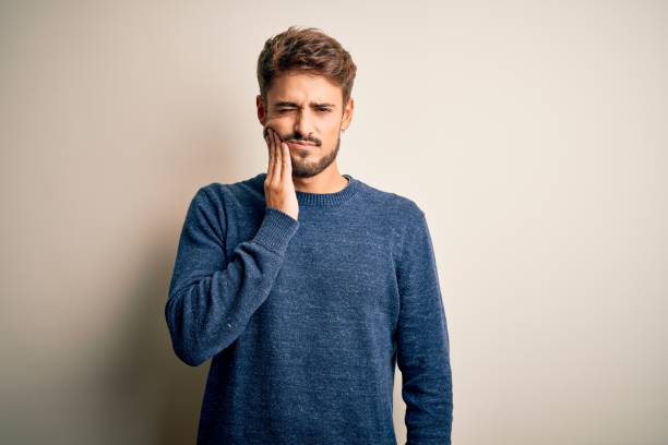 young handsome man with beard wearing casual sweater standing over white background touching mouth with hand with painful expression because of toothache or dental illness on teeth. dentist - dentist pain human teeth toothache imagens e fotografias de stock