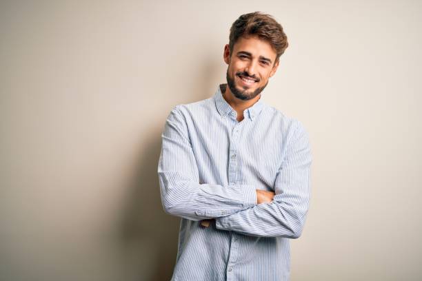 istock Young handsome man with beard wearing striped shirt standing over white background happy face smiling with crossed arms looking at the camera. Positive person. 1212703816