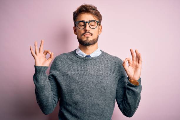 istock Young handsome man with beard wearing glasses and sweater standing over pink background relax and smiling with eyes closed doing meditation gesture with fingers. Yoga concept. 1212706061