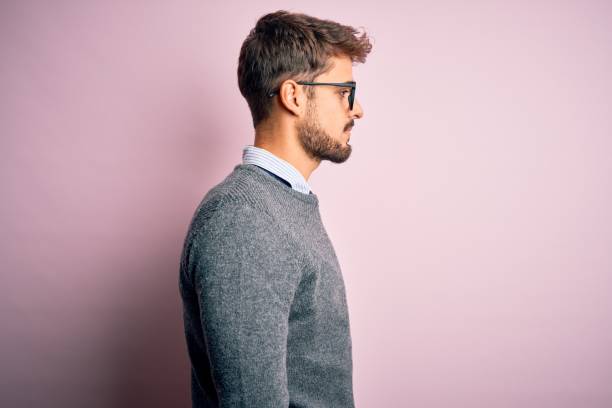 istock Young handsome man with beard wearing glasses and sweater standing over pink background looking to side, relax profile pose with natural face with confident smile. 1212706086