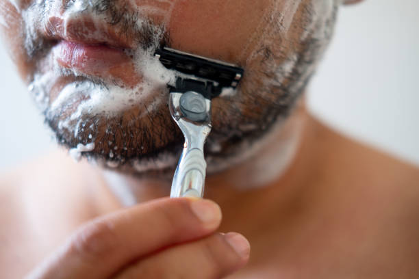 istock Young man with foam soap on his cheeks is standing and removing mustache by shaving from his face. 1212707430
