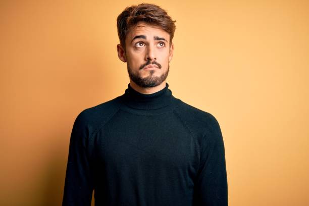 istock Young handsome man with beard wearing turtleneck sweater standing over yellow background smiling looking to the side and staring away thinking. 1212707940