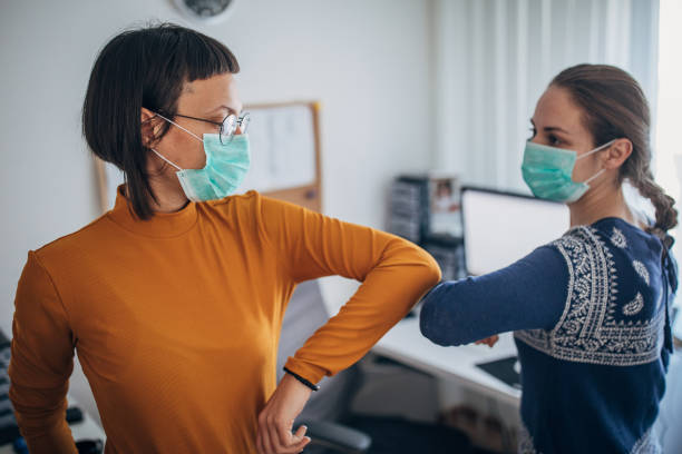 istock Two colleagues at work greeting with alternative handshake in the office ,wearing face mask to protect themselves in the time of coronavirus pandemic 1212708075