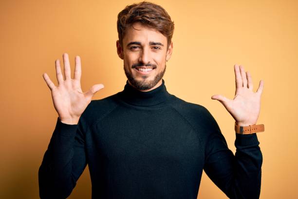 istock Young handsome man with beard wearing turtleneck sweater standing over yellow background showing and pointing up with fingers number ten while smiling confident and happy. 1212708273