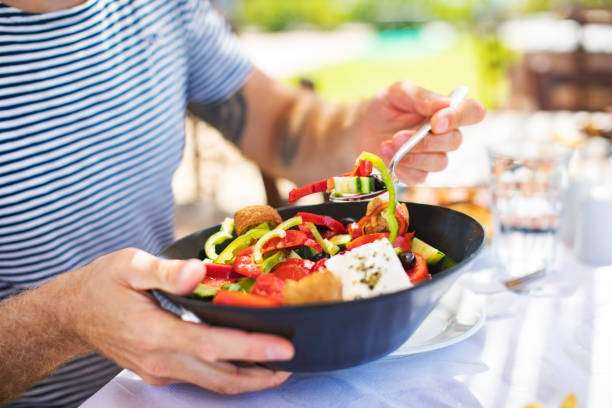 uomini che mangiano insalata greca - greek cuisine greek culture food table foto e immagini stock