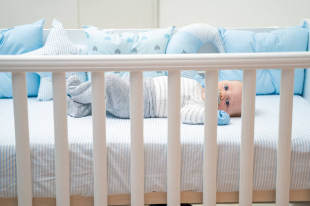 istock Cute baby lying in his crib sucking on pacifier looking at camera 1212709533