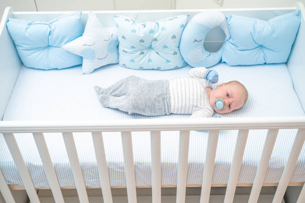 istock Cute baby lying in his crib sucking on pacifier looking at camera top view 1212710678
