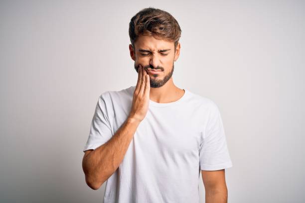 jovem homem bonito com barba vestindo camiseta casual em pé sobre fundo branco tocando boca com mão com expressão dolorosa por causa de dor de dente ou doença dentária nos dentes. dentista - dentist pain human teeth toothache - fotografias e filmes do acervo