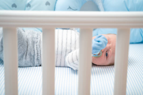 istock Cute baby lying in his crib sucking on pacifier looking at camera close-up 1212711971