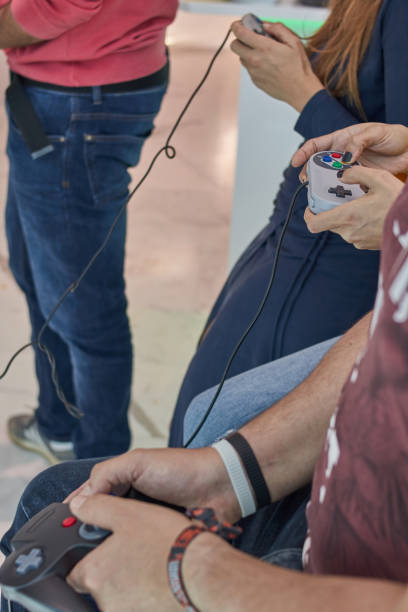 istock Two women and two men playing with retro joysticks connected to an old console for playing retro games with red, purple and yellow 1212717802
