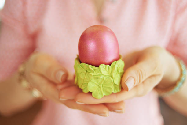 Closeup on woman at home in sunny spring day showing red easter egg in green egg cup.