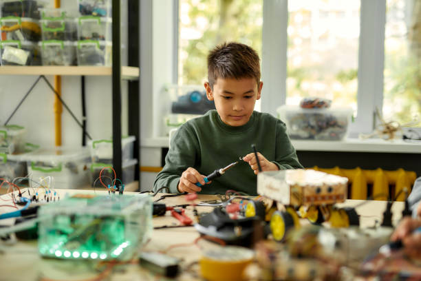 istock Young professional. Asian boy using soldering iron to join chips and wires while making his own vehicle at a stem robotics class. Inventions and creativity for children. 1212724647