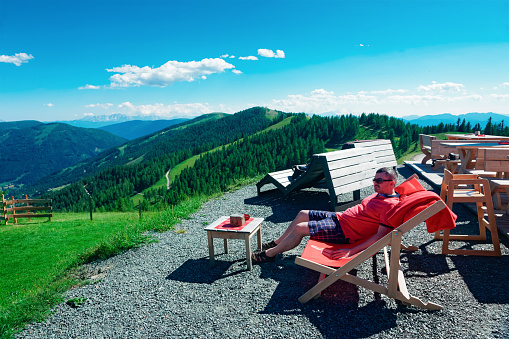 Man at deck chair in Alps mountains and blue sky in Bad Kleinkirchheim, Carinthia of Austria. Tourist relaxing at Austrian hills. Nature landscape. Travel and tourism in summer