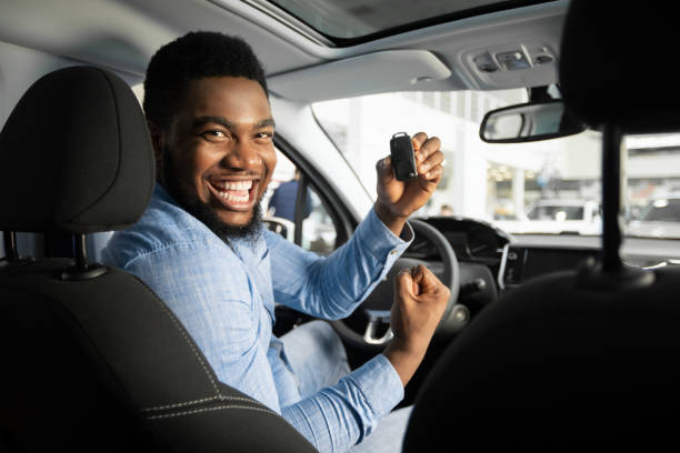 ragazzo gioioso che tiene la chiave automatica che scuote i pugni seduti in auto - car african descent shopping car dealership foto e immagini stock