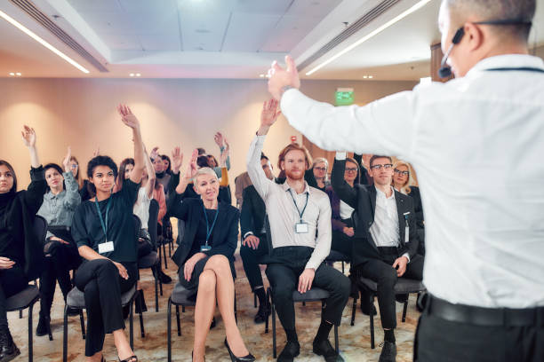Audience listening to asian male speaker and raising hands to ask a question at the conference hall. Man answering questions while giving a talk at corporate business meeting, forum. Selective focus esté preparado. audiencia escuchando a un orador masculino asiático y levantando la mano para hacer una pregunta en la sala de conferencias. hombre respondiendo preguntas mientras da una charla en la reunión de negocios corporativos, foro