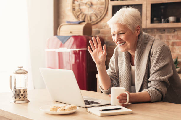 istock Elderly woman making video call on laptop in kitchen 1212728856