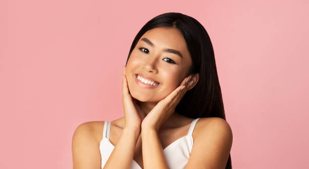 istock Beautiful Asian Girl Touching Face Smiling Posing On Pink Background 1212739933