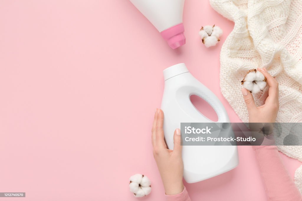 Woman taking care about white wool clothes with eco washing Woman taking care about white wool clothes with eco washing detergent and cotton flowers on pink background. Bio Laundry day Backgrounds Stock Photo
